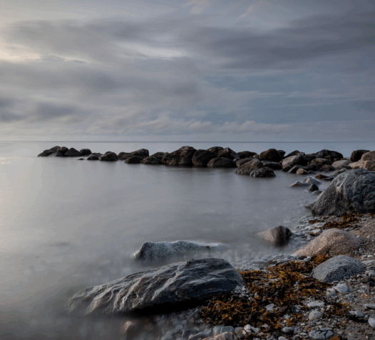 Klippor vid havet under en molnig himmel med stilla vatten.