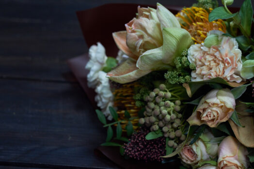 En bukett med olika blommor, inklusive rosor och gröna blad, ligger mot en mörk bakgrund.