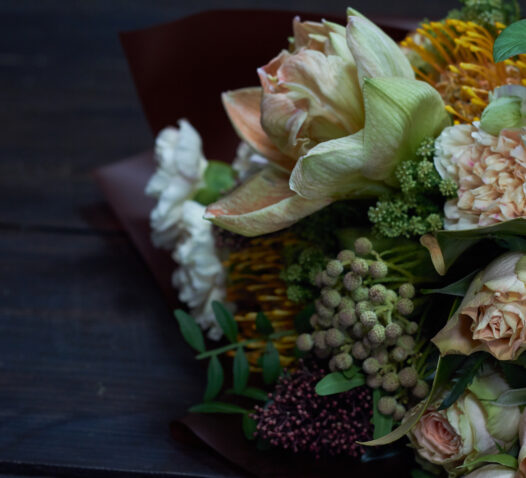 En bukett med olika blommor, inklusive rosor och gröna blad, ligger mot en mörk bakgrund.