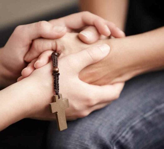Händer som håller varandra med ett träkrucifix i fokus.