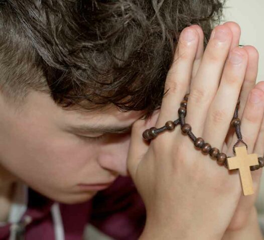 Person med händerna ihop i bön, håller ett radband med kors.